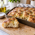 Golden sourdough focaccia with olive oil and flaky sea salt on a wooden board