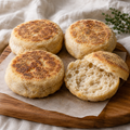 Four jumbo sourdough English muffins, with one split open to show the airy crumb.